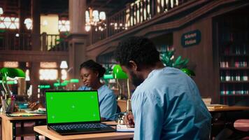 Black medical student reviews case files in the library next to copy space screen, preparing for a lecture or study session on medical practices. Med school pupil learns for a career. Camera A. video