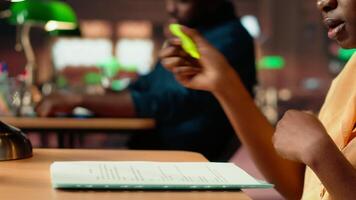 African american scholar highlighting the relevant information from class notes, creating a summary with highlighter pen. Student underlining key words and phrases from the course. Camera B. video