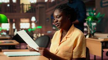Female scholar engrossed in her studies at a university library desk with notebooks and papers, consulting the academic database for exam preparations. Knowledge and self improvement. Camera B. video