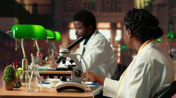Female college student focuses on medical science by using a microscope, examining the chemical processes of microorganisms. Woman studying for her academic thesis paper. Camera B. video