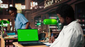 Med school student works on his thesis next to isolated mockup display in the library, doing medical research and reviewing specialty books. Future doctor studies with dedication. Camera A. video