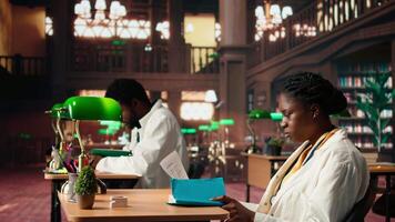 African american female med student reviewing healthcare case files with different diagnostics, learning about the medical practice and methods. Woman scholar reading academic books. Camera A. video