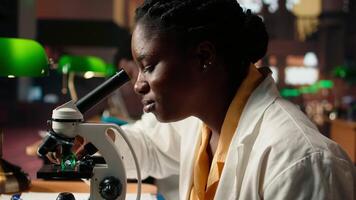 Future researcher works on her thesis by examining microorganisms under the microscope lenses, reading about microbiology and medical science. Focus on scientific exams. Close up. Camera A. video