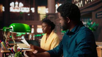 Black college students comparing their class notes at the university library, scholars team studying and consulting information from copy books. Pupils preparing for their upcoming exams. Camera A. video
