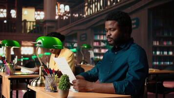 University student researches academic topics in a traditional library, using the classic study space to review lessons and organize course materials. Completing class notes for exams. Camera A. video