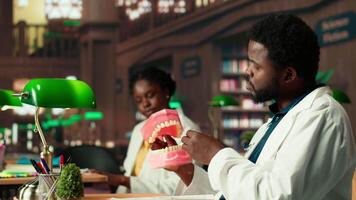 Medical student practices dentistry techniques with a plastic jaw model in a classic library, doing physical research for stomatology thesis. Developing professional skills for the career. Camera B. video