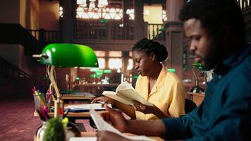 African american scholars reading course notes and comparing information at the library, studying for a test together using academic database for research. Educational materials. Camera A. video