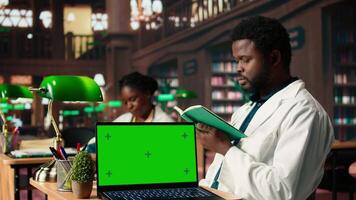 Medical student uses books in the campus study space next to green screen, combining research, anatomy lessons and academic methods. Pupil reading research papers for medical practice. Camera A. video
