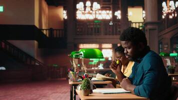 African american pupil underlining key words and phrases at the library, creating a summary with the highlighter pen at a university campus study space. Academic research for exams. Camera A. video