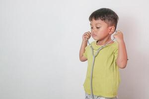 Smiling Asian kid in green medical uniform holding stethoscope looking at camera, healthy concept idea. photo