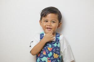 Smiling happy 2-3 year old Asian boy touching his chin, looking to the side, thinking about idea playing game isolated on white background photo