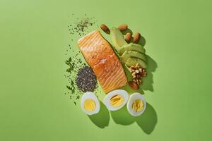 Healthy Food Flatlay Green Background Illustration of Salmon, Avocado, Eggs, Nuts and Seeds photo