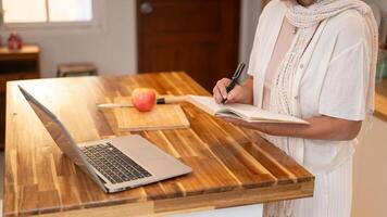 A retired woman writing down ingredients in a book while learning a new recipe on the internet. photo