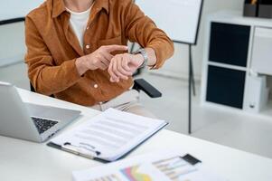 A close-up of a strict businessman points at his wristwatch while looking at his colleagues. photo