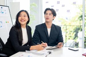Two positive Asian businesspeople are intently listening to a presentation during a meeting. photo