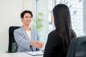 A satisfied Asian businessman shakes hands with a candidate after a job interview in his office. photo