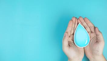 Water drops in hand on blue background with copy space. Concepts of saving water, World Day for Water, conserving environmental resources, and treating wastewater to clean water sources. photo