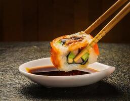 Side View of Sushi Roll with Soy Sauce and Chopsticks in Hand photo