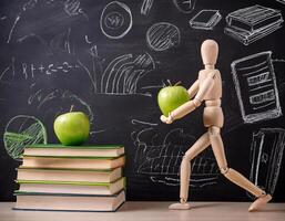 Wooden Mannequin Holding an Apple, Surrounded by Books and Green Blackboard Scribbles photo