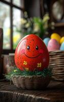 A red painted egg with a smiley face on it sits on a wooden table. The egg is surrounded by grass and flowers, giving it a cheerful and playful appearance photo