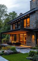 Twilight view of modern house. A contemporary stone house showcases large windows and outdoor seating surrounded by lush greenery at dusk. photo