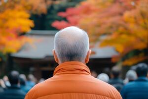 Elderly man in orange jacket enjoys autumn foliage at a shrine during a peaceful gathering in Japan photo