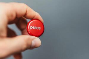 Holding a red peace button, symbolizing hope and unity against a simple background photo