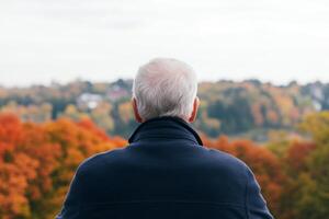 Senior man enjoys a peaceful view of autumn foliage from a hillside overlooking a colorful landscape in the afternoon photo
