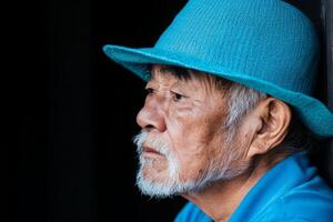 Elderly man wearing a blue hat looks thoughtfully in a dimly lit room during late afternoon photo