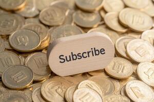 Wooden subscribe button on a pile of coins representing digital currency engagement and commitment in online content photo