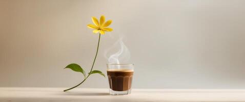 a glass of coffee sits on a table with a yellow flower in the background. photo