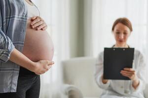 Pregnant woman hands touching big belly in doctor office. Female doctor examining pregnant woman. Gynecologist doctor consulting patient about pregnancy in hospital. Visit to doctor medical checkup photo