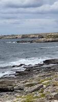 An expansive view of ocean waves crashing against a rugged shore, with elevated cliffs in the background under an overcast sky, creating a tranquil atmosphere for relaxation and photography video