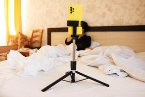 A yellow phone in a stand against the background of a girl in a rumpled bed. Concept of webcam services of an intimate nature via communication. Copy space for text photo