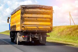 A yellow dump truck transports grain from the fields with a closed awning. Import and export of grain, transportation of agricultural products. Copy space for text photo