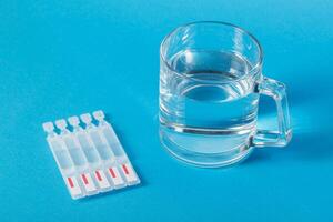 a cup of water and tubes with a new generation metabiotic on a blue background. Treatment of the intestines, restoration of microflora after dysbacteriosis. Copy space for text photo
