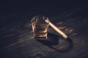 A glass of whiskey and a cigar on a wooden table photo