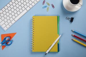 A desk with a yellow notepad, a pencil, a cup of coffee, a computer keyboard photo