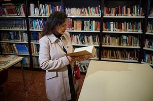 Woman reading a book in a library surrounded by bookshelves and resources photo