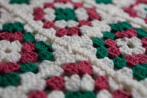 Close up photo of crocheted square motives made of soft wool. Retro style blanket in making. Crochet pattern texture. Beautiful multi-colored plaid crocheted from squares. Crocheted. Granny square