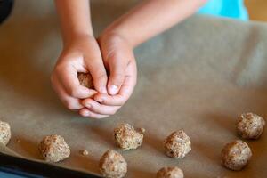 Children's hands make nut cookies and place them on a baking sheet photo