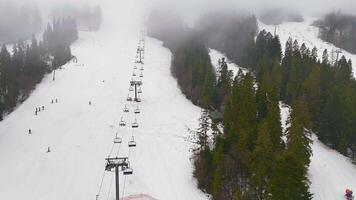 Ski slope with chairlift and forest in fog, A ski slope surrounded by dense forest is seen from above, video
