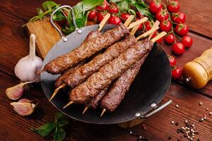 Grilled skewers of marinated meat served with fresh vegetables and spices on a rustic wooden table photo
