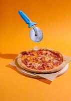 Pizza with vibrant orange background and a pizza cutter floating above ready for slicing photo