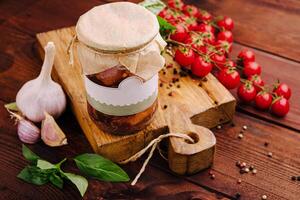 Delicious homemade preserves with garlic, tomatoes, and basil arranged on a rustic wooden board photo