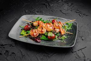Grilled shrimp skewers served on a dark plate with greens and cherry tomatoes in a modern dining setting photo