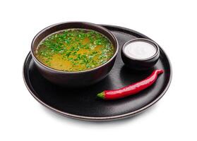 Warm soup with herbs and chili served on a round plate with a side of cream in a small bowl photo