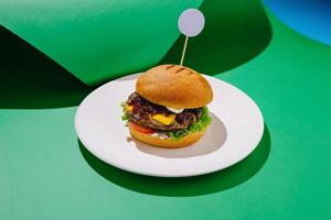 Gourmet hamburger with crispy lettuce, cheese, and tomato served on a white plate against a green backdrop photo
