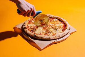 Hand slicing a fresh pizza with a pizza cutter on a vibrant yellow background photo