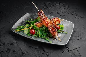 Grilled skewers of marinated meat presented on a stylish plate with fresh greens and cherry tomatoes in a modern setting photo
